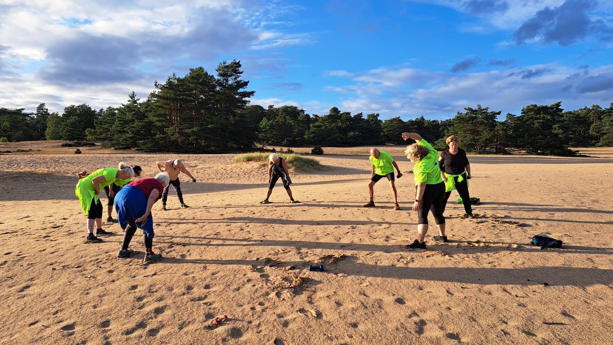 Slow Sports groep in een grote kring aan het trainen op een zandvlakte met bos op de achtergrond.